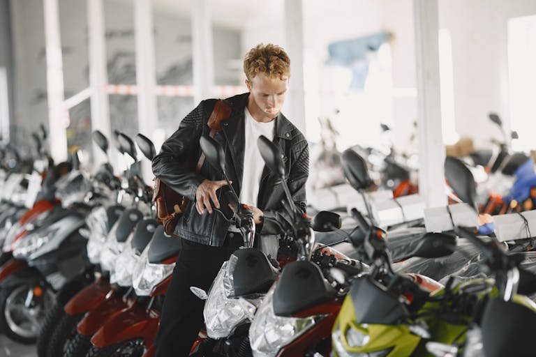 How to Choose Your First Motorcycle A young man examines a row of motorcycles inside a motor dealership, showcasing interest and choice.