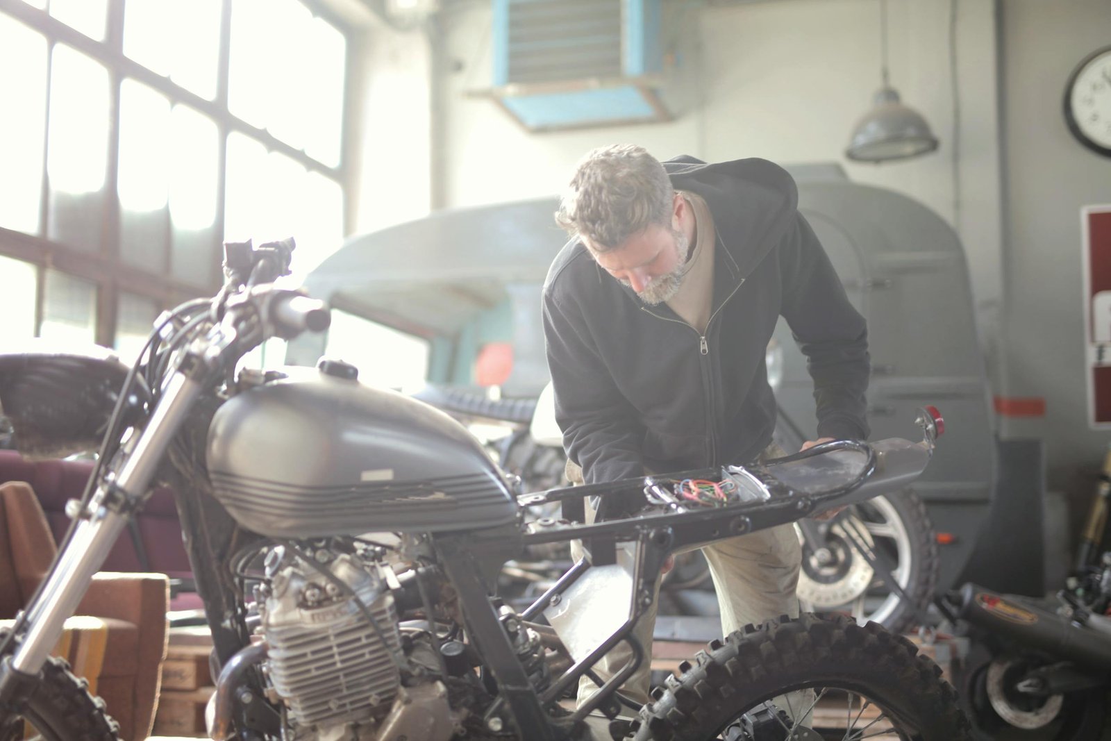 Man working on a motorcycle inside a workshop, focusing on repair and maintenance tasks.